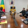 Réunion autour d'une table de conférence dans un bureau ministériel, drapeau du Congo et portraits officiels au mur
